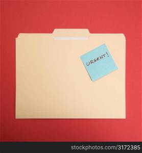 Folder with a sticky note attached reading urgent on a red background.