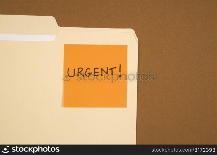 Folder with an orange sticky note attached reading urgent on brown background.