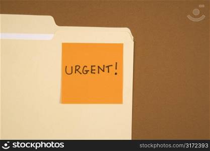 Folder with an orange sticky note attached reading urgent on brown background.