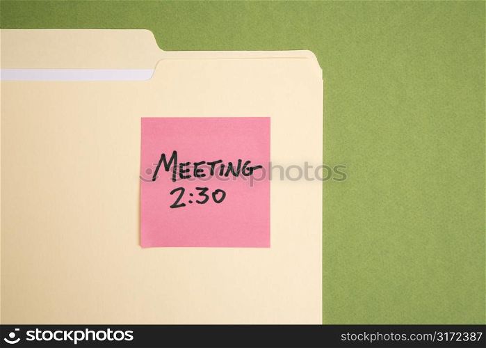 Folder with pink sticky note reminder for a meeting on a green background.