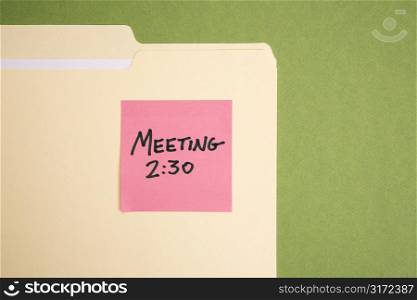 Folder with pink sticky note reminder for a meeting on a green background.