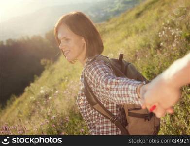 Follow me. Beautiful young laughing woman holds the hand of a man on sunny field