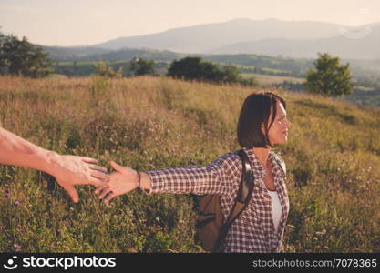 Follow me. Beautiful young laughing woman holds the hand of a man on sunny field