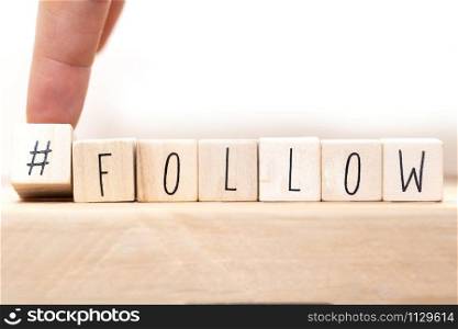 Follow sign made of cubes on a wooden table with Hashtag near white background, socialmedia concept close-up. Follow sign made of cubes on a wooden table with Hashtag near white background, socialmedia concept