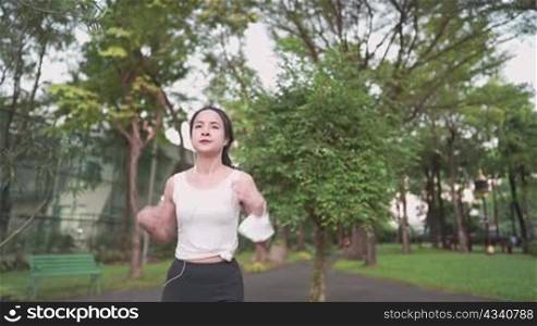 Follow up view of sportive asian young black hair woman running through camera in city park on public green background, fit attractive pretty woman jogging at outdoor workout on background of trees