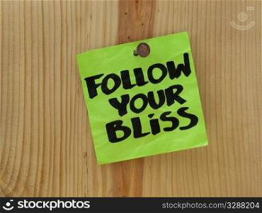 follow your bliss handwriting on a green sticky note nailed to wooden wall or plank