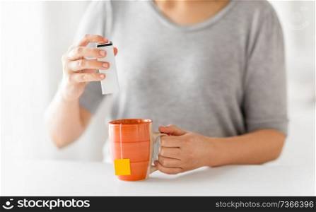 food additives and drinks concept - close up of woman adding sweetener to cup of tea. close up of woman adding sweetener to cup of tea