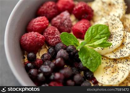 food and breakfast concept - close up of cereals in bowl with wild berries, banana and peppermint on slate stone table. cereal breakfast with berries, banana and mint