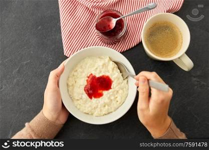 food and breakfast concept - hands of woman with spoon eating porridge in bowl with fruit jam and cup of coffee on slate stone table. hands with porridge breakfast and cup of coffee