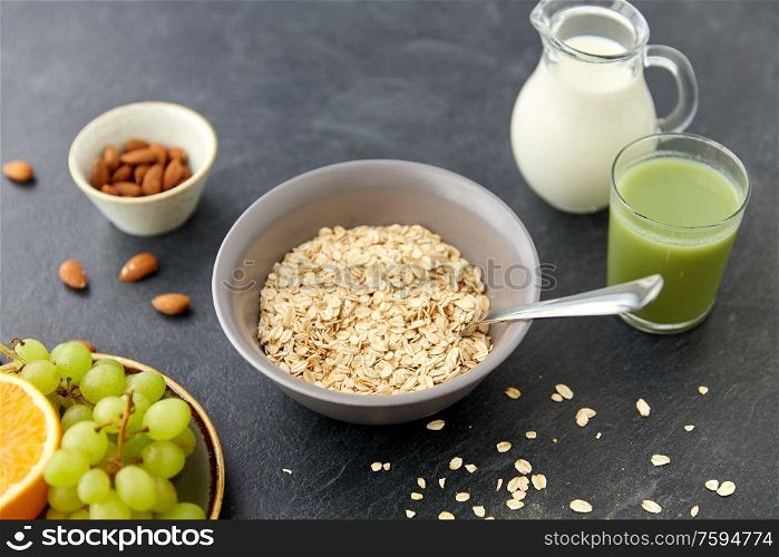 food and breakfast concept - oatmeal cereals in bowl, fruits, almond nuts, glass of juice and jug with milk on slate stone table. oatmeal with fruits, almond nuts and jug of milk