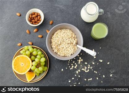 food and breakfast concept - oatmeal cereals in bowl, fruits, almond nuts, glass of juice and jug with milk on slate stone table. oatmeal with fruits, almond nuts and jug of milk