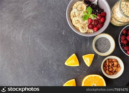 food and breakfast concept - oatmeal cereals in bowl with wild berries, fruits, almond nuts and poppy seeds on slate stone table. cereal with berries, fruits, nuts and poppy seeds