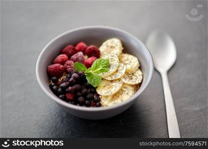 food and breakfast concept - oatmeal cereals in bowl with wild berries, banana and spoon on slate stone table. cereal breakfast with berries, banana and spoon
