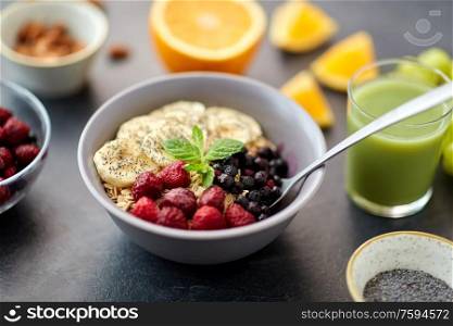 food and breakfast concept - oatmeal cereals in bowl with wild berries, banana, spoon and glass of juice on slate stone table. cereal breakfast with berries, banana and spoon