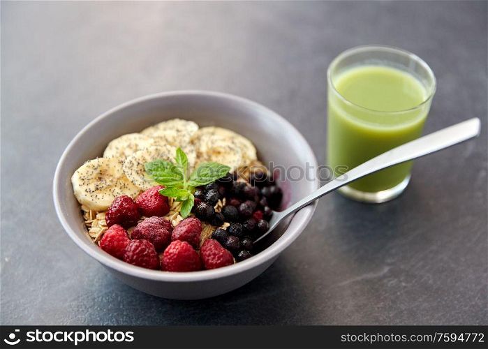 food and breakfast concept - oatmeal cereals in bowl with wild berries, banana, spoon and glass of juice on slate stone table. cereal breakfast with berries, banana and spoon
