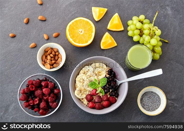 food and breakfast concept - oatmeal cereals in bowl with wild berries, fruits and glass of juice on slate stone table. cereal with berries, fruits and glass of juice
