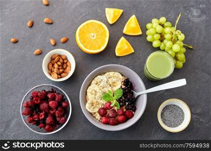 food and breakfast concept - oatmeal cereals in bowl with wild berries, fruits and glass of juice on slate stone table. cereal with berries, fruits and glass of juice