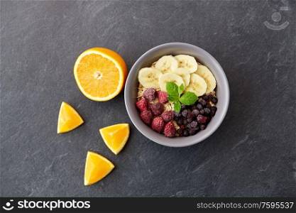 food and breakfast concept - oatmeal cereals in bowl with wild berries, fruits and peppermint on slate stone table. cereal with wild berries, fruits and peppermint