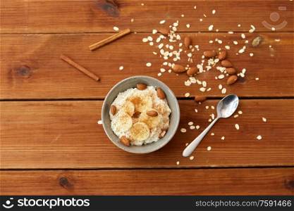 food and breakfast concept - oatmeal porridge in bowl with sliced banana, almond nuts and cinnamon on wooden table. oatmeal with banana and almond on wooden table