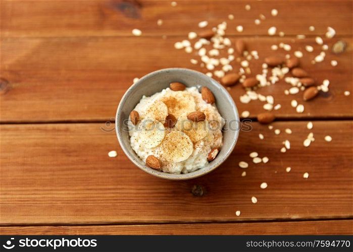 food and breakfast concept - oatmeal porridge in bowl with sliced banana, almond nuts and cinnamon on wooden table. oatmeal with banana and almond on wooden table