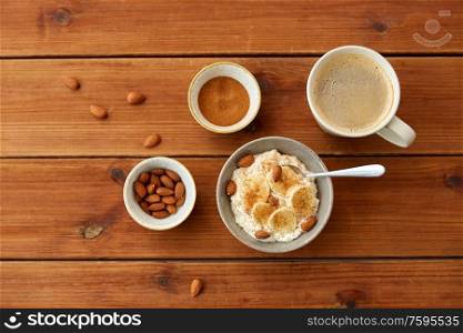 food and breakfast concept - oatmeal porridge in bowl with sliced banana, almond nuts and cinnamon and cup of coffee on wooden table. oatmeal with banana and almond on wooden table