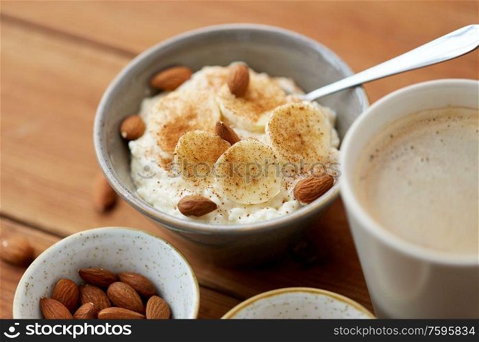 food and breakfast concept - oatmeal porridge in bowl with sliced banana, almond nuts and cinnamon and cup of coffee on wooden table. oatmeal with banana and almond on wooden table