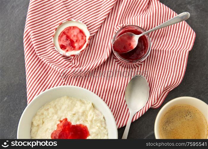 food and breakfast concept - porridge in bowl with jam, spoon and cup of coffee on slate stone table. porridge breakfast with jam, spoon and coffee