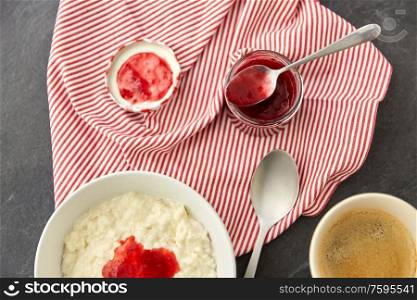 food and breakfast concept - porridge in bowl with jam, spoon and cup of coffee on slate stone table. porridge breakfast with jam, spoon and coffee