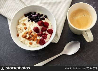 food and breakfast concept - porridge in bowl with wild berries, almond nuts, spoon and cup of coffee on slate stone table. porridge breakfast with berries, almonds and spoon