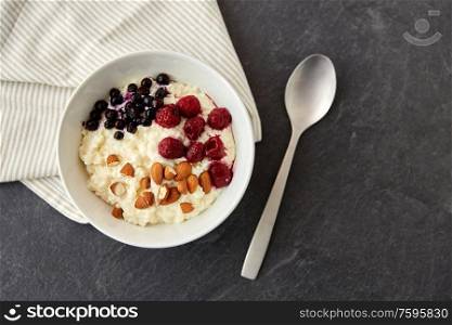 food and breakfast concept - porridge in bowl with wild berries, almond nuts and spoon on slate stone table. porridge breakfast with berries, almonds and spoon