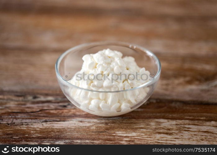 food and dairy products concept - close up of homemade cottage cheese in glass bowl on wooden table. close up of cottage cheese in bowl on wooden table