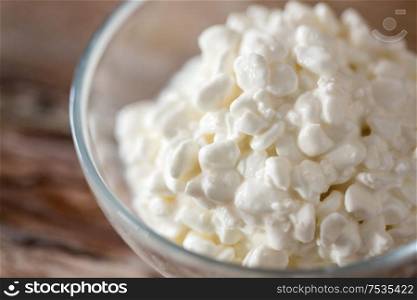 food and dairy products concept - close up of homemade cottage cheese in glass bowl on wooden table. close up of cottage cheese in bowl on wooden table