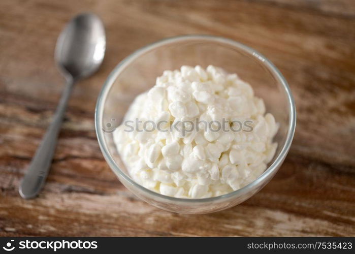 food and dairy products concept - close up of homemade cottage cheese in glass bowl on wooden table. close up of cottage cheese in bowl on wooden table