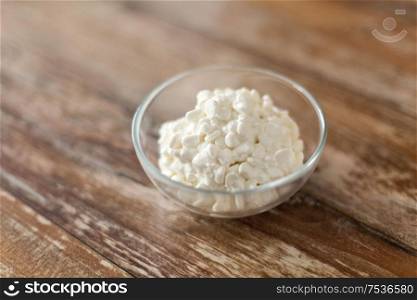 food and dairy products concept - close up of homemade cottage cheese in glass bowl on wooden table. close up of cottage cheese in bowl on wooden table