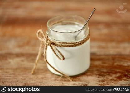 food and dairy products concept - close up of homemade yogurt or sour cream in vintage glass jar on wooden table. yogurt or sour cream in glass jar on wooden table