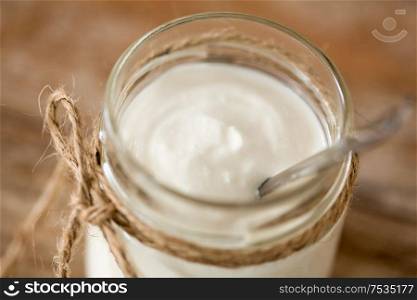 food and dairy products concept - close up of homemade yogurt or sour cream in vintage glass jar on wooden table. yogurt or sour cream in glass jar on wooden table
