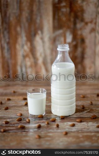 food and dairy products concept - glass and bottle of milk and almond nuts on wooden table. milk and almonds on wooden table