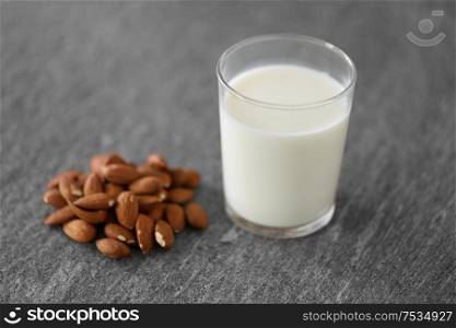food and dairy products concept - glass of lactose free milk and almonds on stone table. glass of lactose free milk and almonds on table