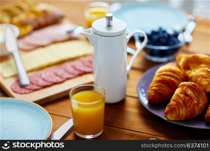 food and drinks concept - coffee pot and glass of orange juice on wooden table at breakfast. coffee pot, juice and food on table at breakfast