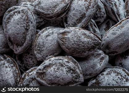 Food and drinks: large group of unpeeled roasted apricot kernels, arranged as abstract background. Unpeeled roasted apricot kernels, in a round wooden bowl
