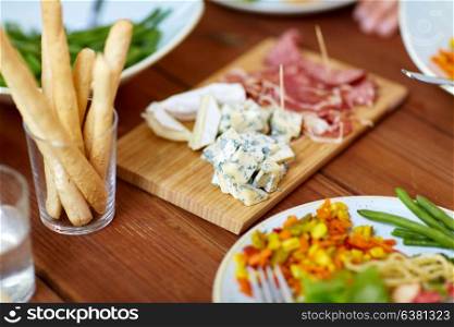food and eating concept - blue cheese, breadsticks and jamon or parma ham on wooden table. blue cheese and breadsticks on table