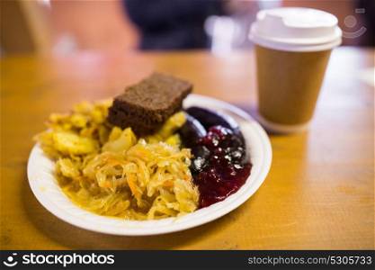 food and eating concept - braised cabbage, potato, rye bread and sausages with cranberry sauce on plate. braised cabbage and sausages with sauce on plate