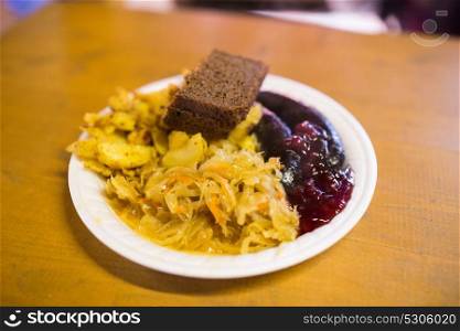 food and eating concept - braised cabbage, potato, rye bread and sausages with cranberry sauce on plate. braised cabbage and sausages with sauce on plate