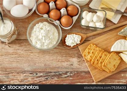 food and eating concept - close up of cottage cheese, crackers, yogurt with butter and chicken eggs on wooden table. cottage cheese, crackers, eggs, yogurt and butter