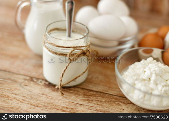 food and eating concept - close up of cottage cheese, jug of milk, homemade yogurt and chicken eggs on wooden table. cottage cheese, yogurt, milk and chicken eggs