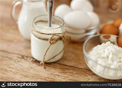 food and eating concept - close up of cottage cheese, jug of milk, homemade yogurt and chicken eggs on wooden table. cottage cheese, yogurt, milk and chicken eggs