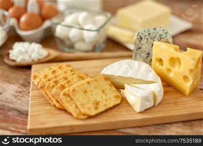 food and eating concept - close up of salty crackers and cheese on wooden board. crackers, cheese and other food on wooden board