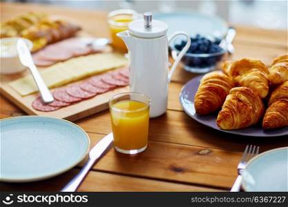 food and eating concept - coffee pot and glass of orange juice on served wooden table at breakfast. coffeepot and glass of juice on table at breakfast
