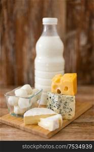 food and eating concept - different kinds of cheese and milk on wooden board. different kinds of cheese and milk on wooden board