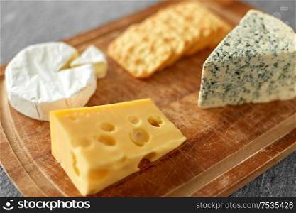 food and eating concept - different kinds of cheese and salty crackers on wooden cutting board. different cheeses and crackers on wooden board